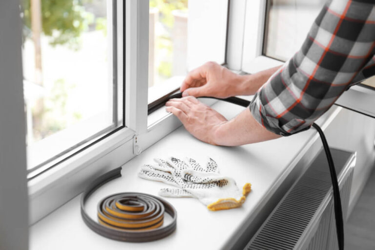 person in flannel shirt installing sealing strip to their apartment window