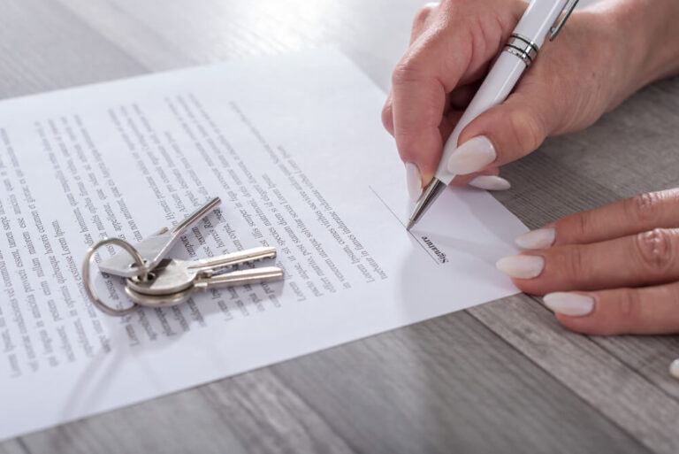 close up of someone signing their renewal lease with a set of keys on top of the document