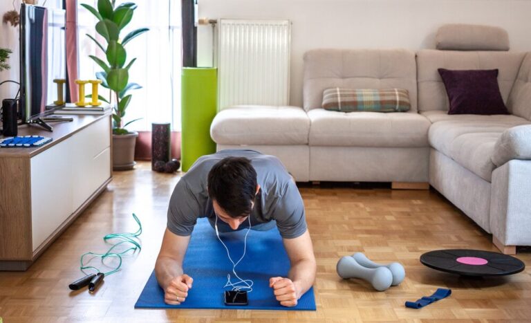 man planks on a yoga mat surrounded with light workout equipment