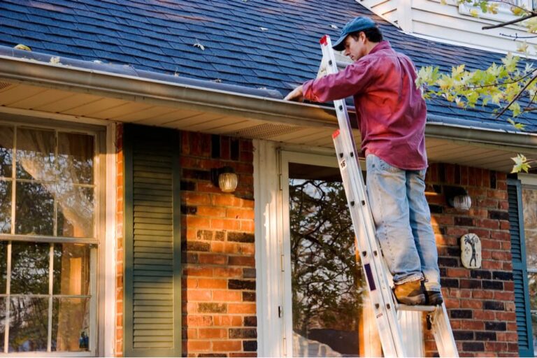 man on ladder cleaning the gutter of a home rental